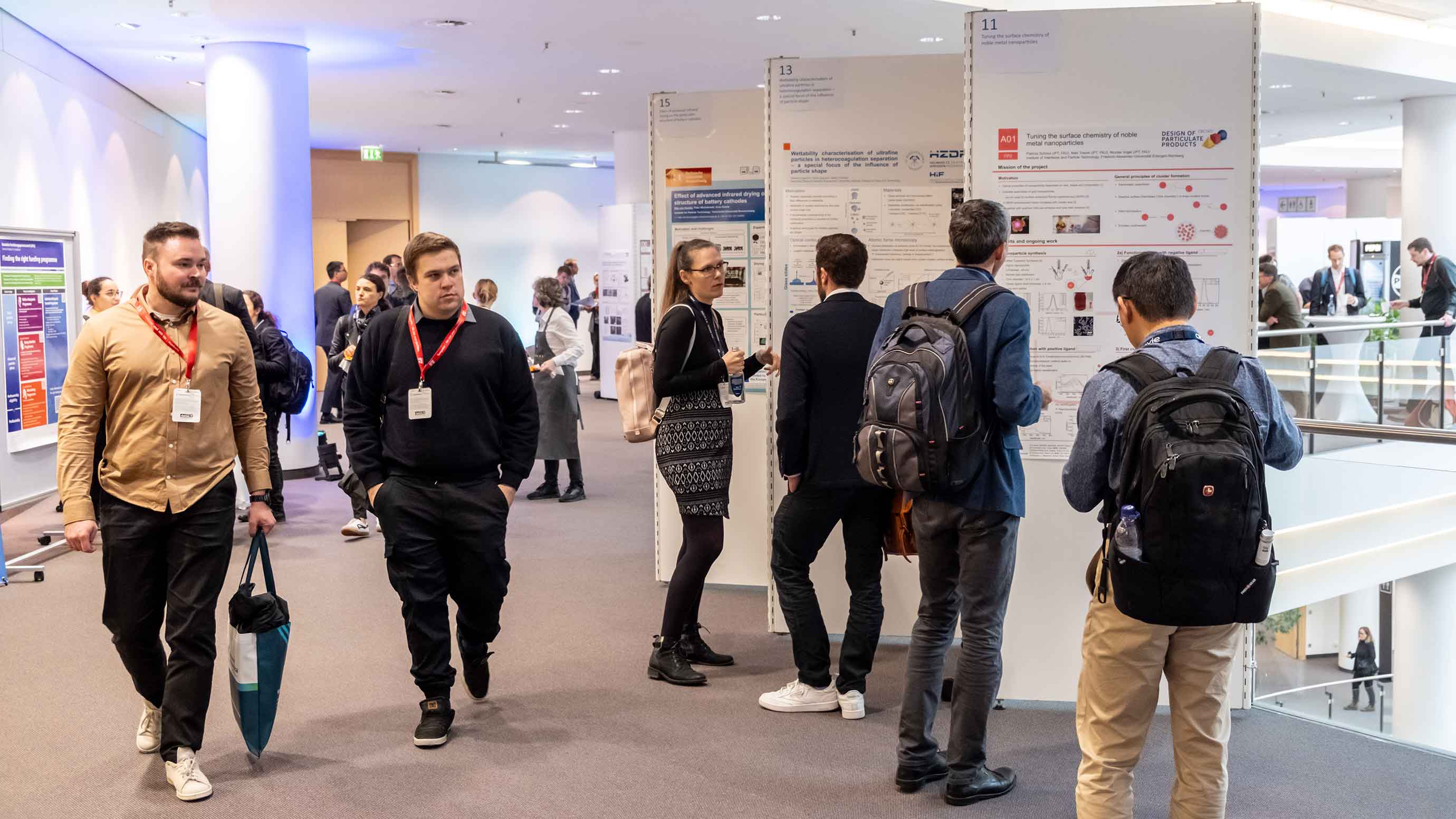 Conference attendees view and discuss research posters in a bright, modern indoor setting.